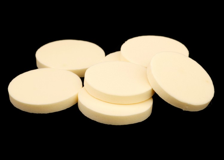 A studio shot of seven ordinary cosmetic sponges: cream foam rubber, about two inches in diameter, sold in packages for disposable use.