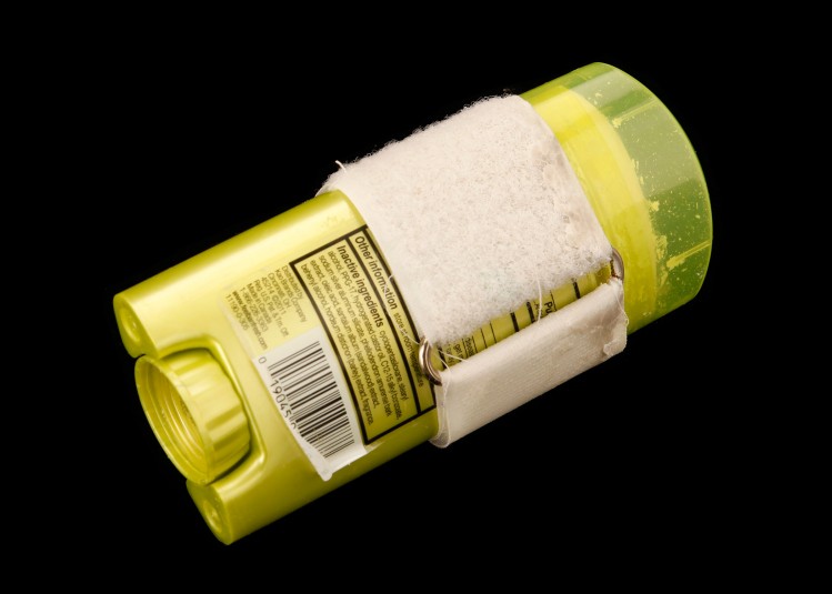 Back side of the deodorant stick, showing the white velcro and a metal clip that holds the velcro in place and makes it adjustable to fit around different objects.