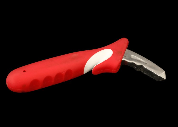 A red handle tool with a white indentation where there is a internal blade for slicing a seat belt in an emergency. One end of the tool has a piece of metal protruding out to be inserted into a car’s metal door-latch.