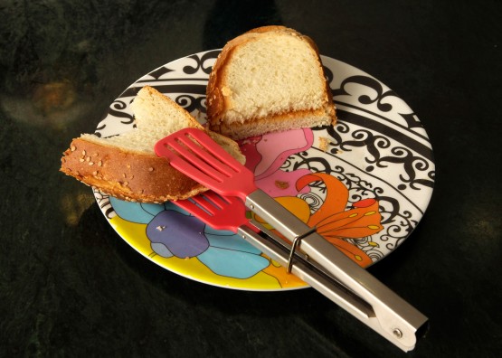The salad tongs in use, gripping a sandwich half on a plate. The square hold makes it possible for Cindy to tune the openness between tongs, adjustable to the type of food and size of bite. The small size of the whole tool makes it possible get food from the plate to the mouth without undue awkward distance.
