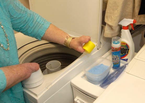 In Cindy's laundry room, Cindy stands with the yellow cup ready to dispense detergent in a way adapted to her body.