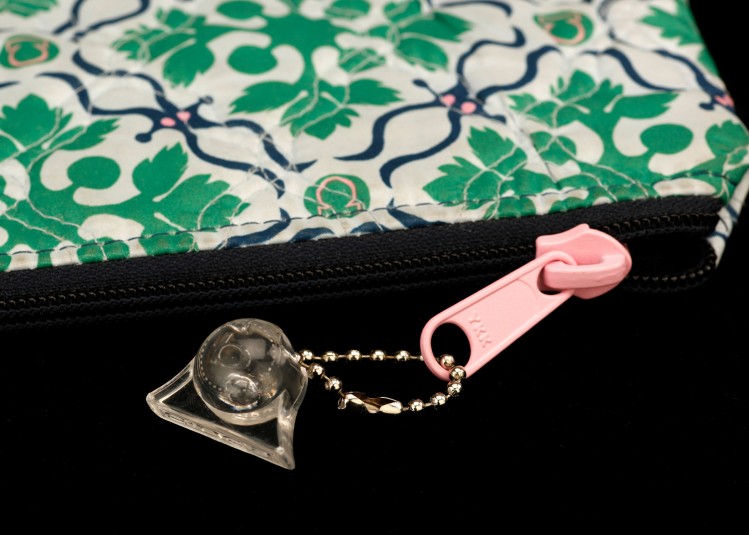 A  close-up of a metal linked key chain with a clear plastic fob on it. Key chain is attached to a pink zipper pull on a flowered purse.